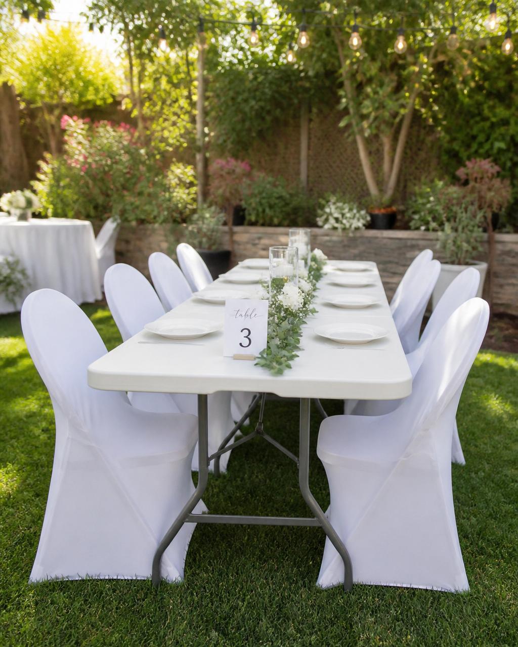 White plastic folding table and chairs with white chair covers in a garden party setting
